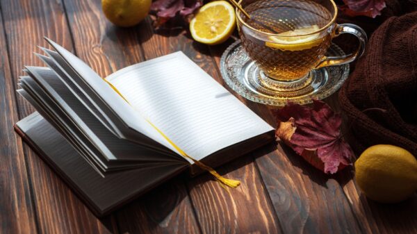 Open notebook with blank pages on a wooden table, accompanied by a hot cup of lemon tea, a warm sweater, and vibrant autumn leaves, creating a cozy atmosphere in morning light